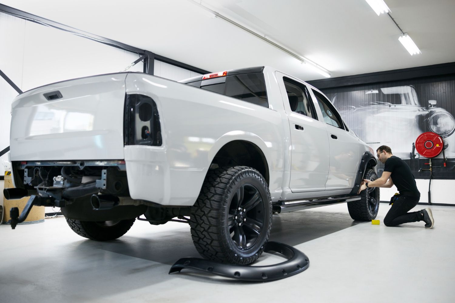 A man is kneeling down next to a white truck in a garage.
