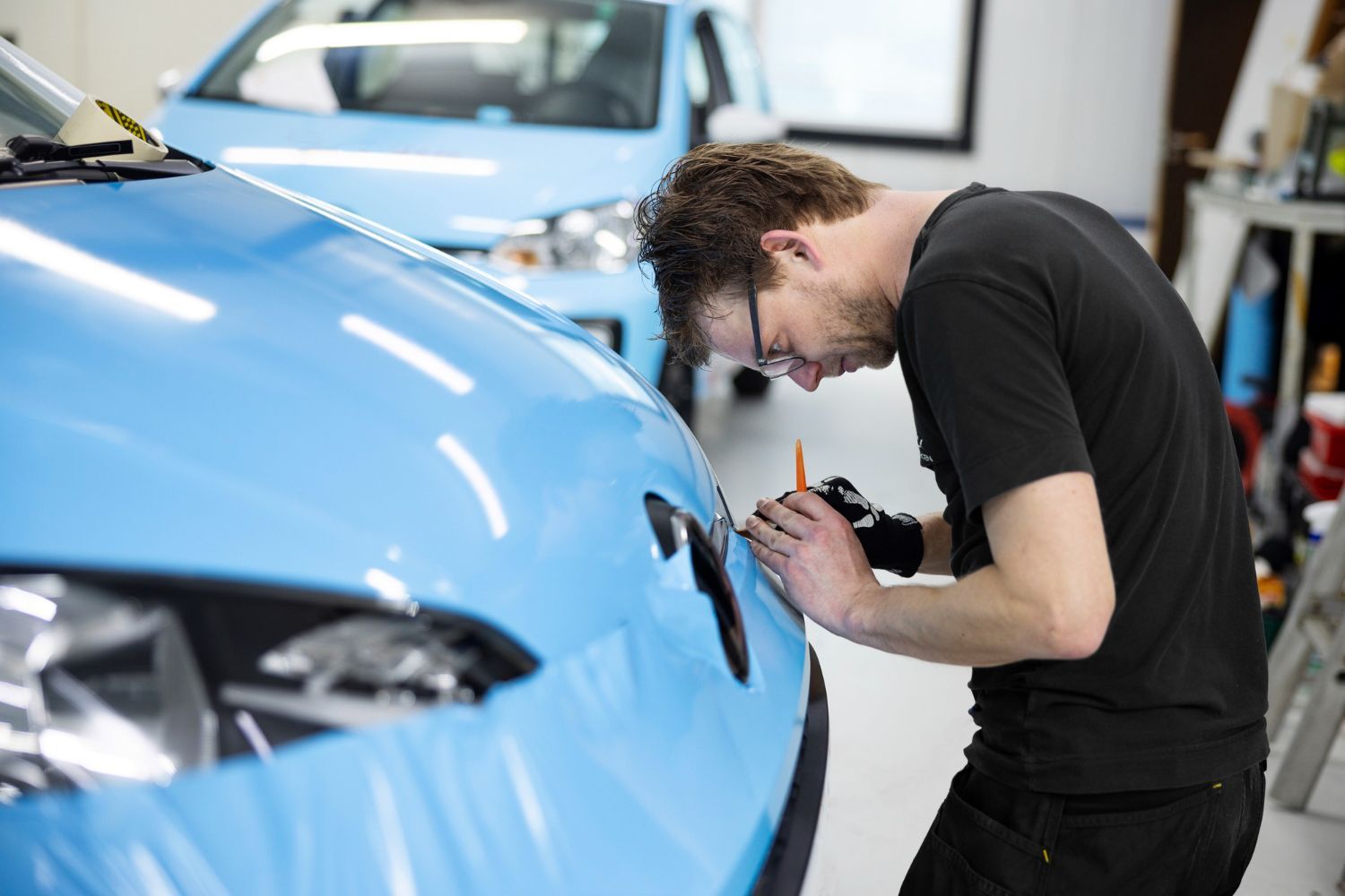 A man is working on a blue car in a garage.
