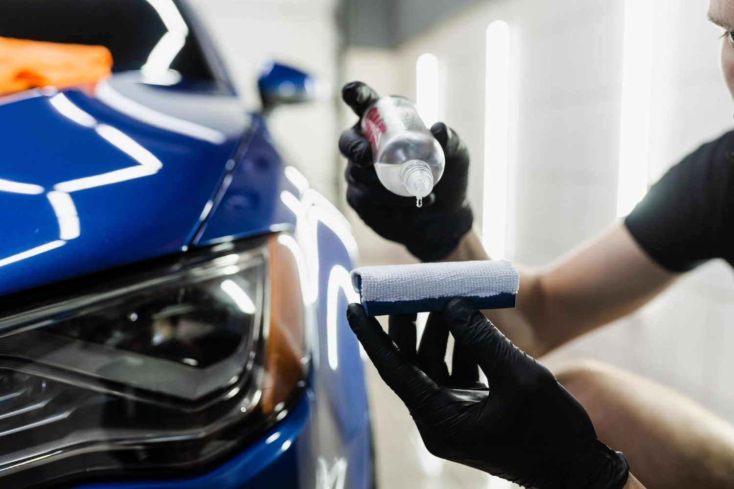 A person is applying ceramic coating to a blue car.