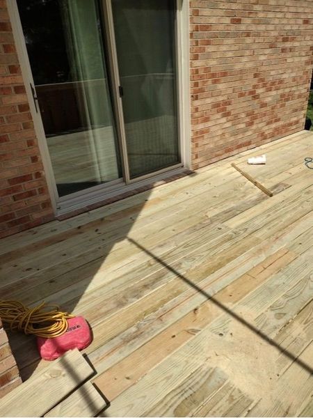 Wooden deck next to a brick wall and sliding glass door. Tools and coiled electrical cord are visible.