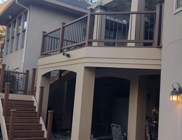 Two-story house with a wooden deck and brown railing. Stairs lead up to the deck. The exterior is beige.