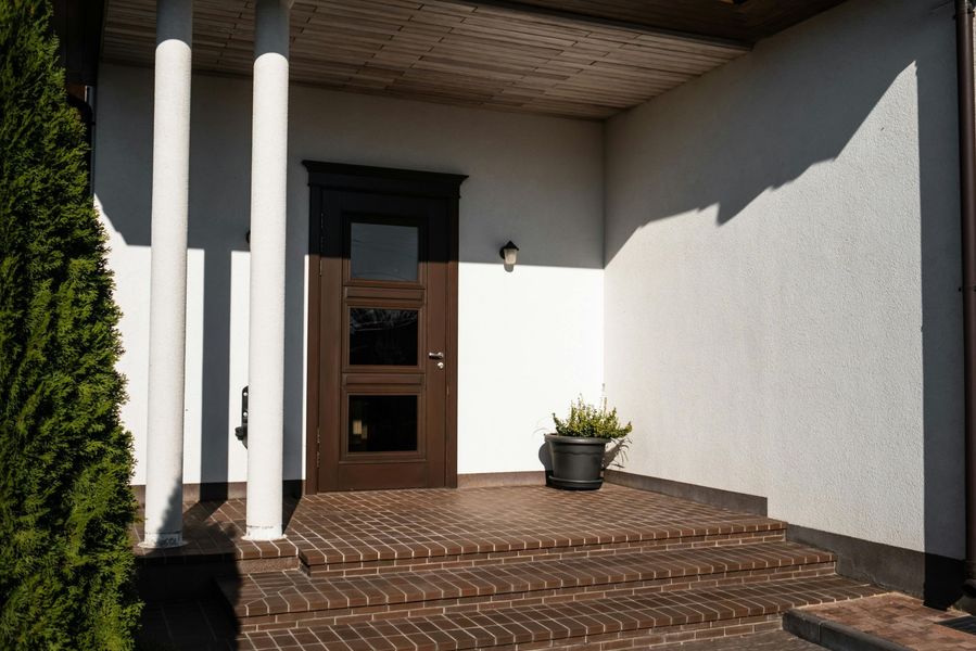 Brown front door with glass panels, flanked by white columns, leading to a brick patio.