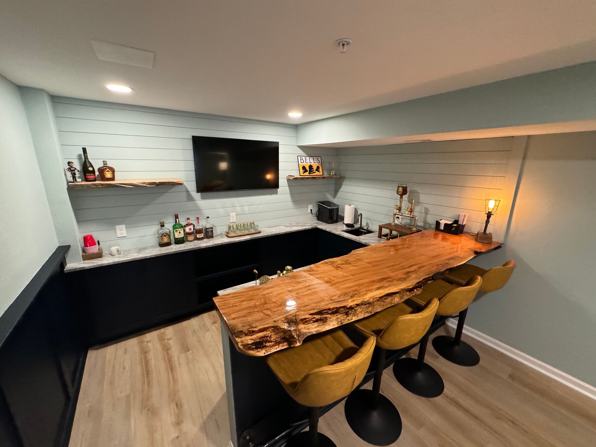 A kitchen with a wooden bar and stools and a flat screen tv.