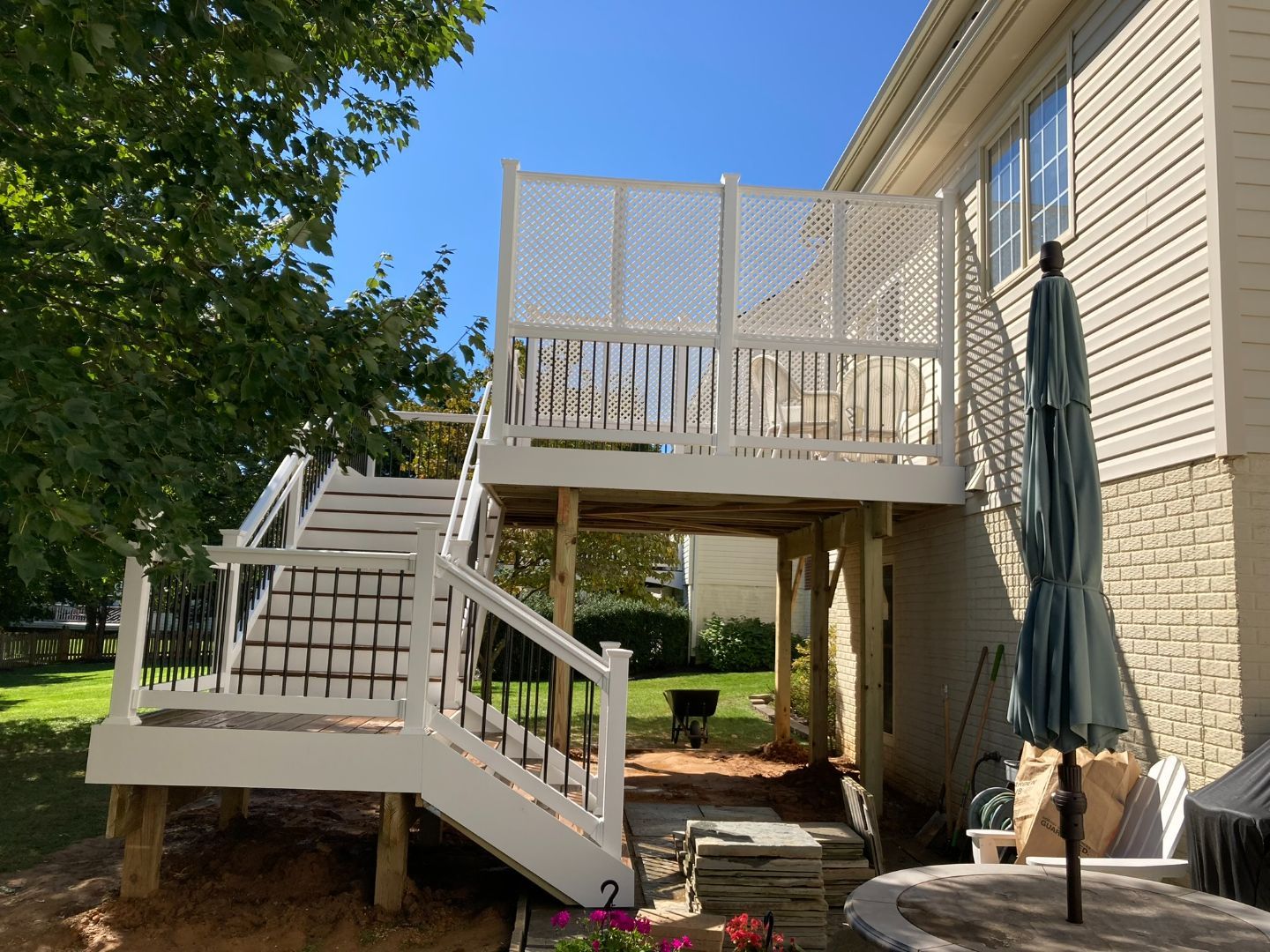 A white deck with stairs and an umbrella in front of a house.