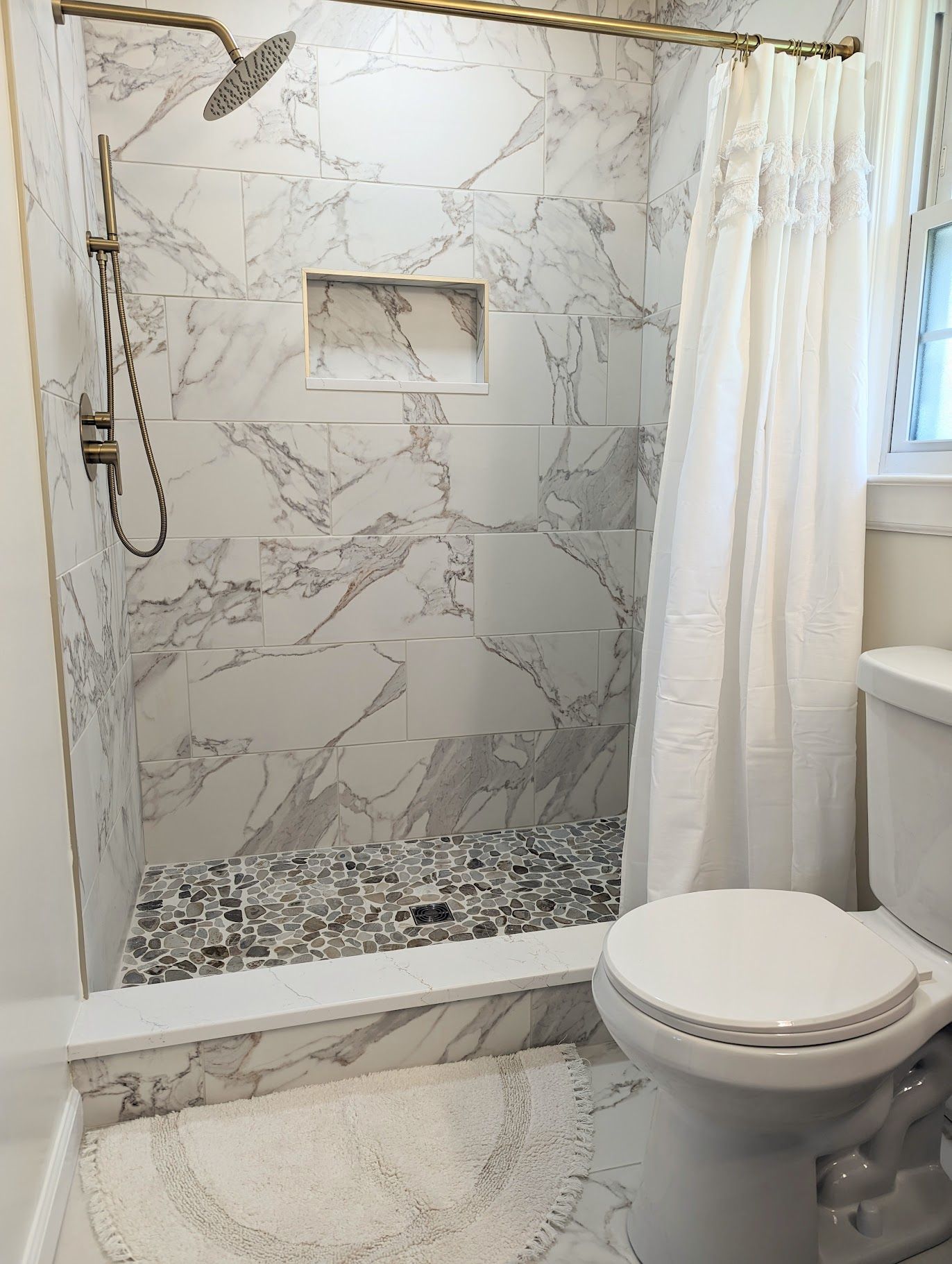 A bathroom with a toilet , shower , and marble tiles.