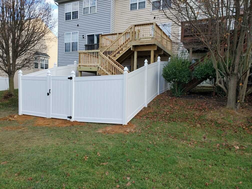 A white fence surrounds a backyard with a deck and stairs.