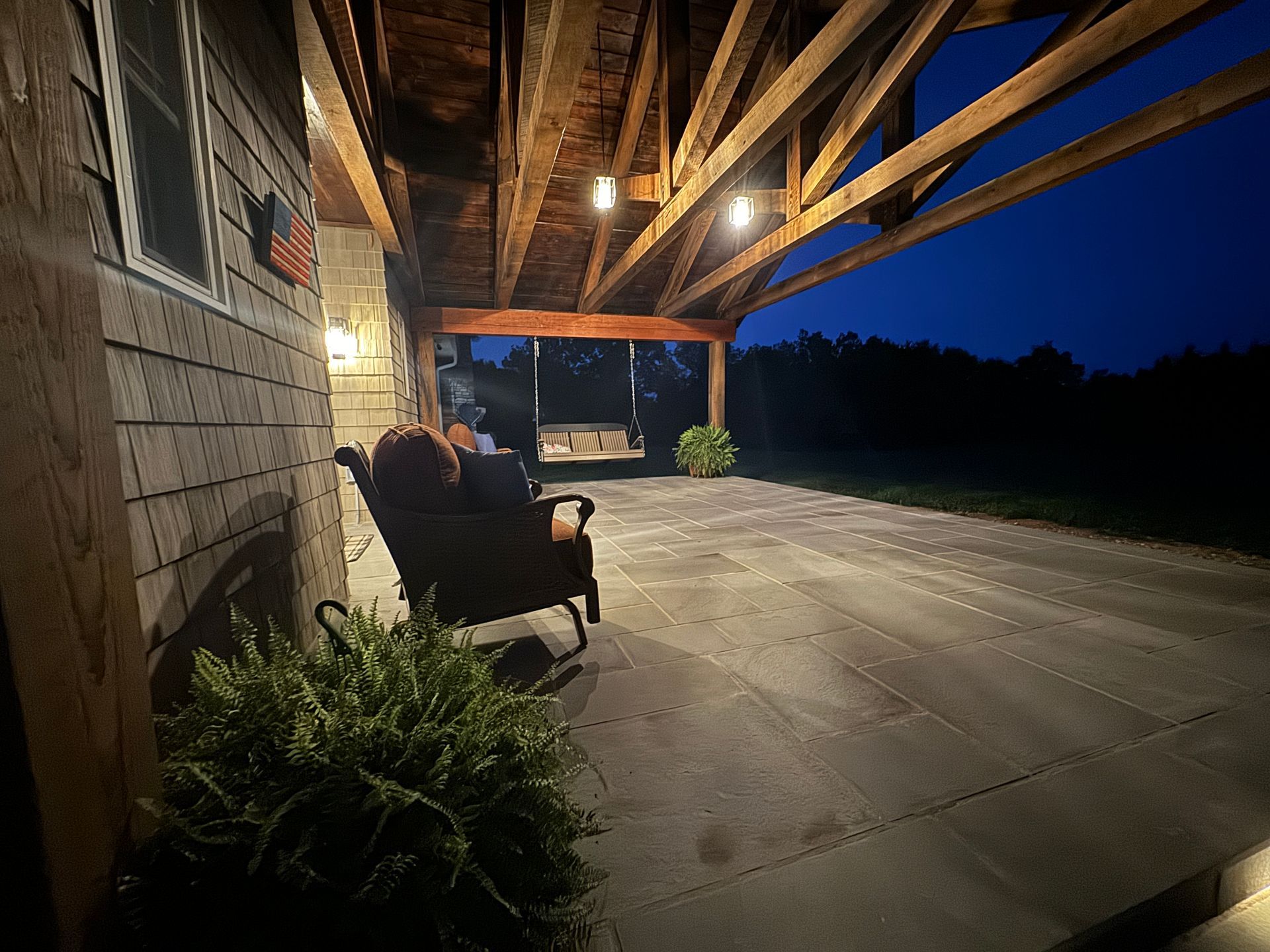 A patio with a bench and chairs under a covered porch at night.