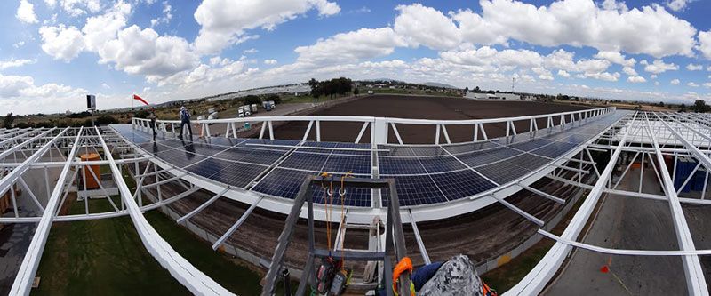 Paneles solares instalados sobre una estructura metálica blanca, bajo un cielo azul nublado. Se ven trabajadores en el tejado.industria solar