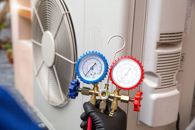 A person is holding a gauge in front of an air conditioner.