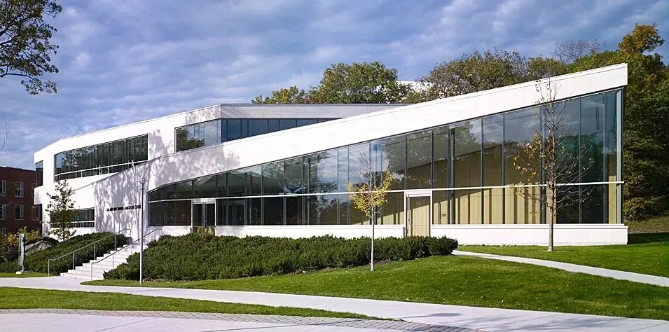 Modern glass-and-white office building with large windows, surrounded by lawn and trees under a blue sky