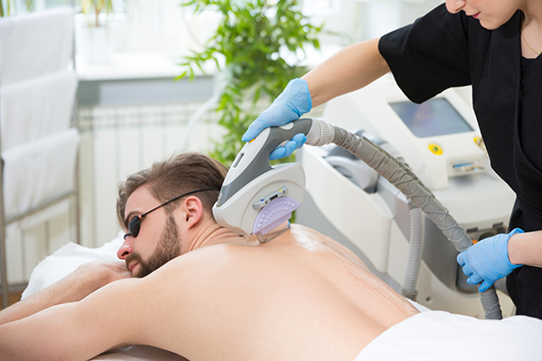 Mann erhält in einem Spa eine Laser-Haarentfernung auf dem Rücken, unterstützt von Mona Larcher