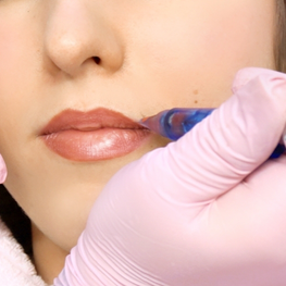 Person, die ein Permanent Make-Up Behandlung bei den Lippen erhält. Hand mit rosa Handschuh hält den Tätowierstift.