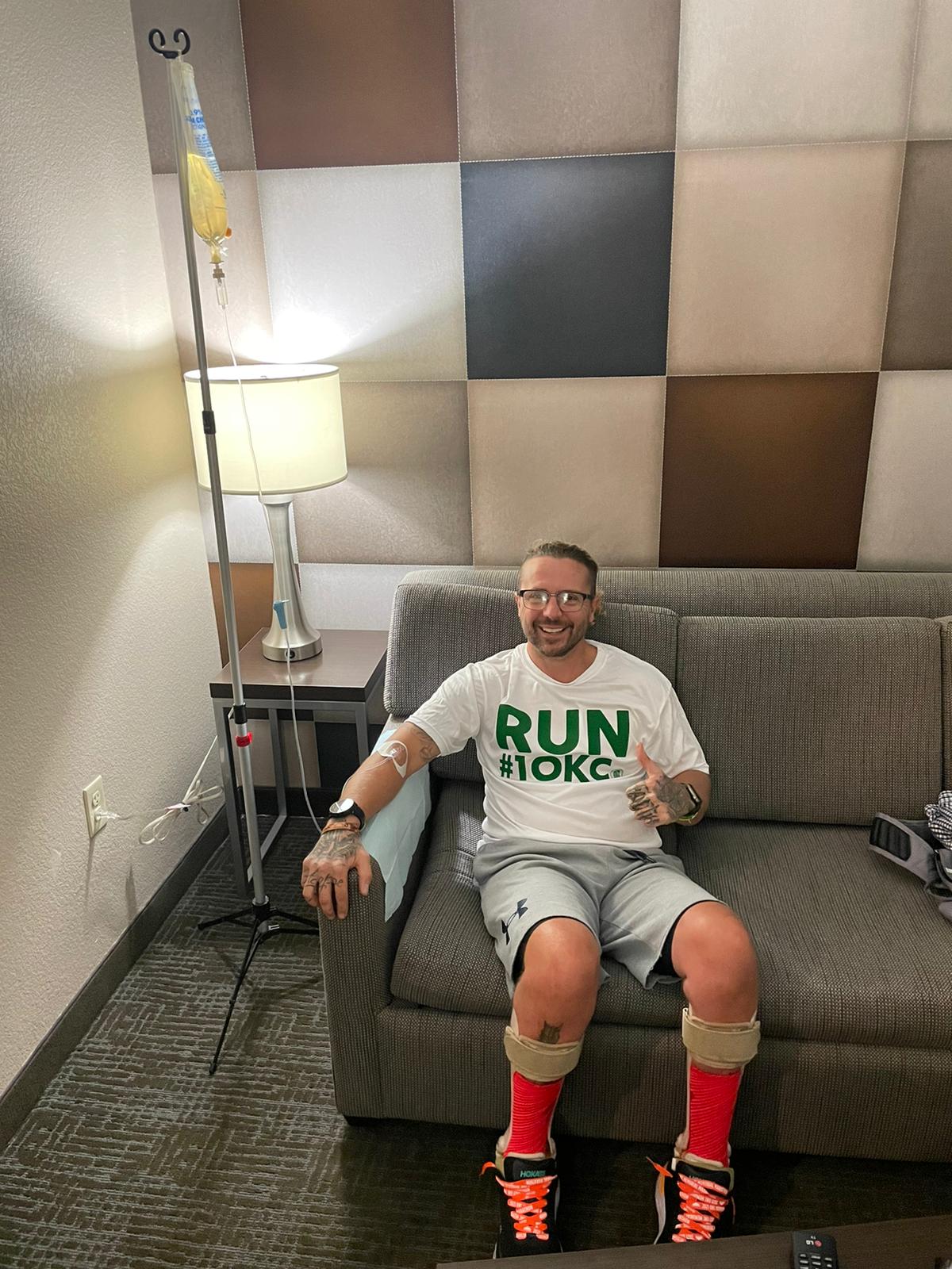 A man is sitting on a couch wearing a shirt that says run okc.