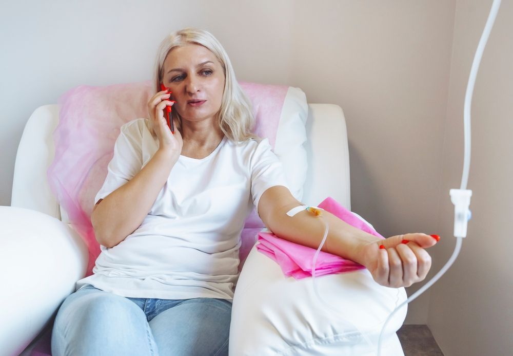 A woman is sitting on a couch with an iv in her hand and talking on a cell phone.