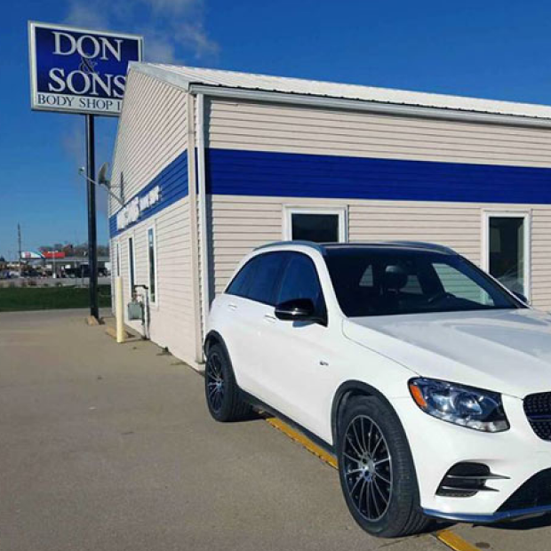 A white car is parked in front of a building that says don sons | Don & Sons Body Shop