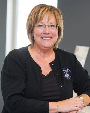 A woman wearing glasses and a black sweater is smiling for the camera. | Don & Sons Body Shop