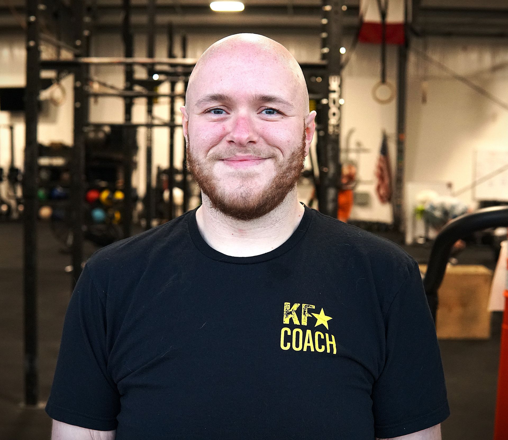 Man with a beard in a gym, wearing a black shirt that says 