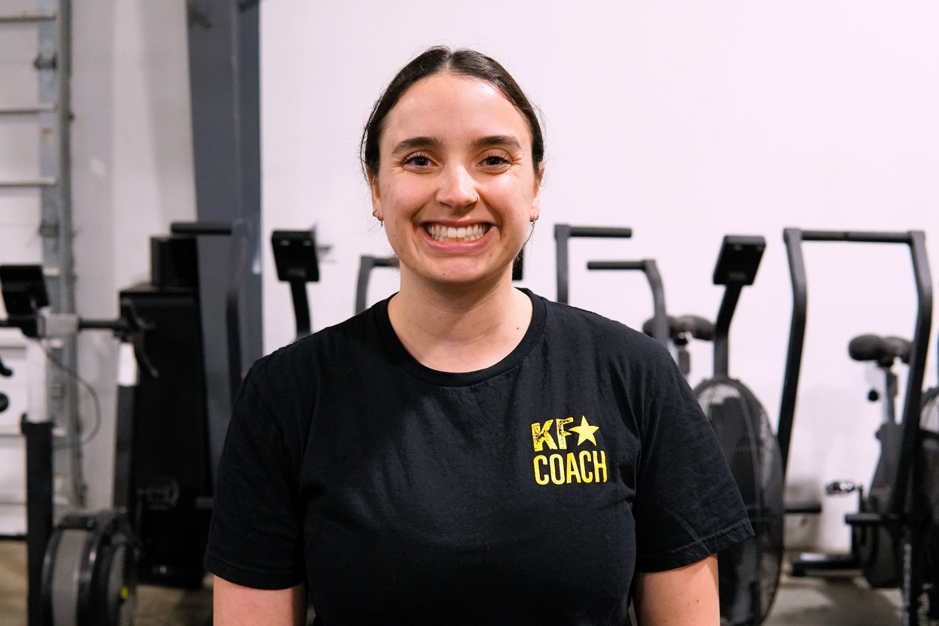 Woman smiling in a gym, wearing a black shirt that says 