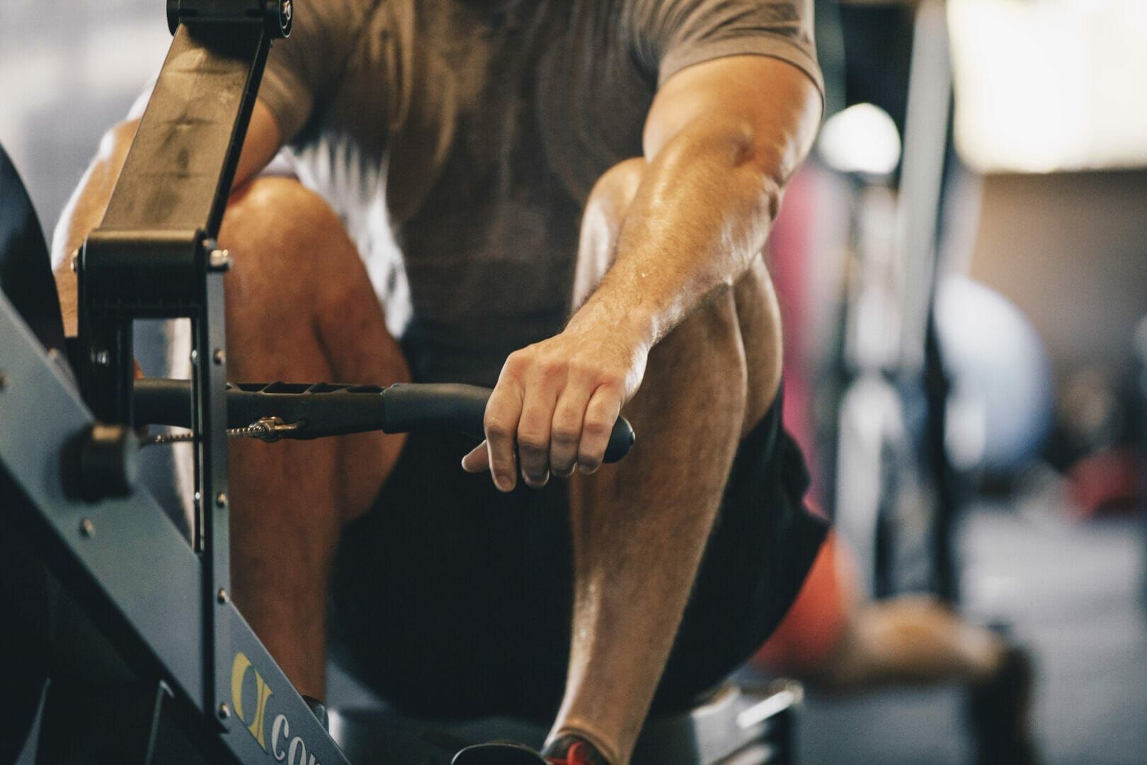 Man using a rowing machine at a gym, holding handle, focus on arms.
