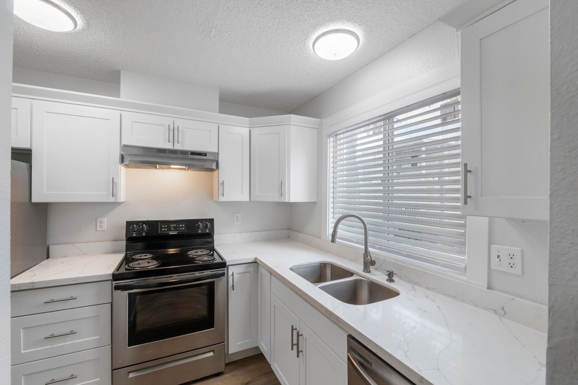 A kitchen with white cabinets , stainless steel appliances , a sink and a window.