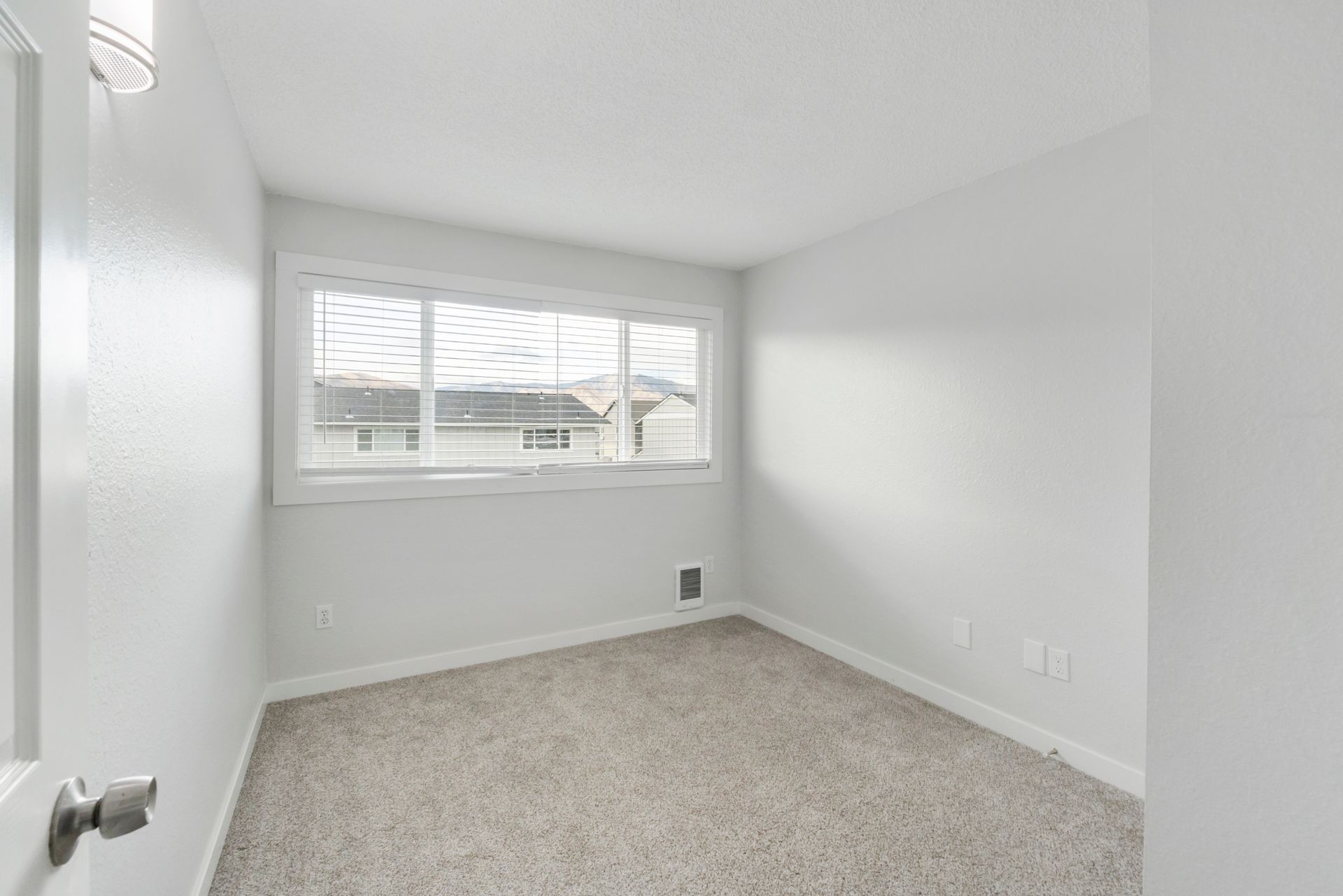 An empty bedroom with a large window and a carpeted floor.