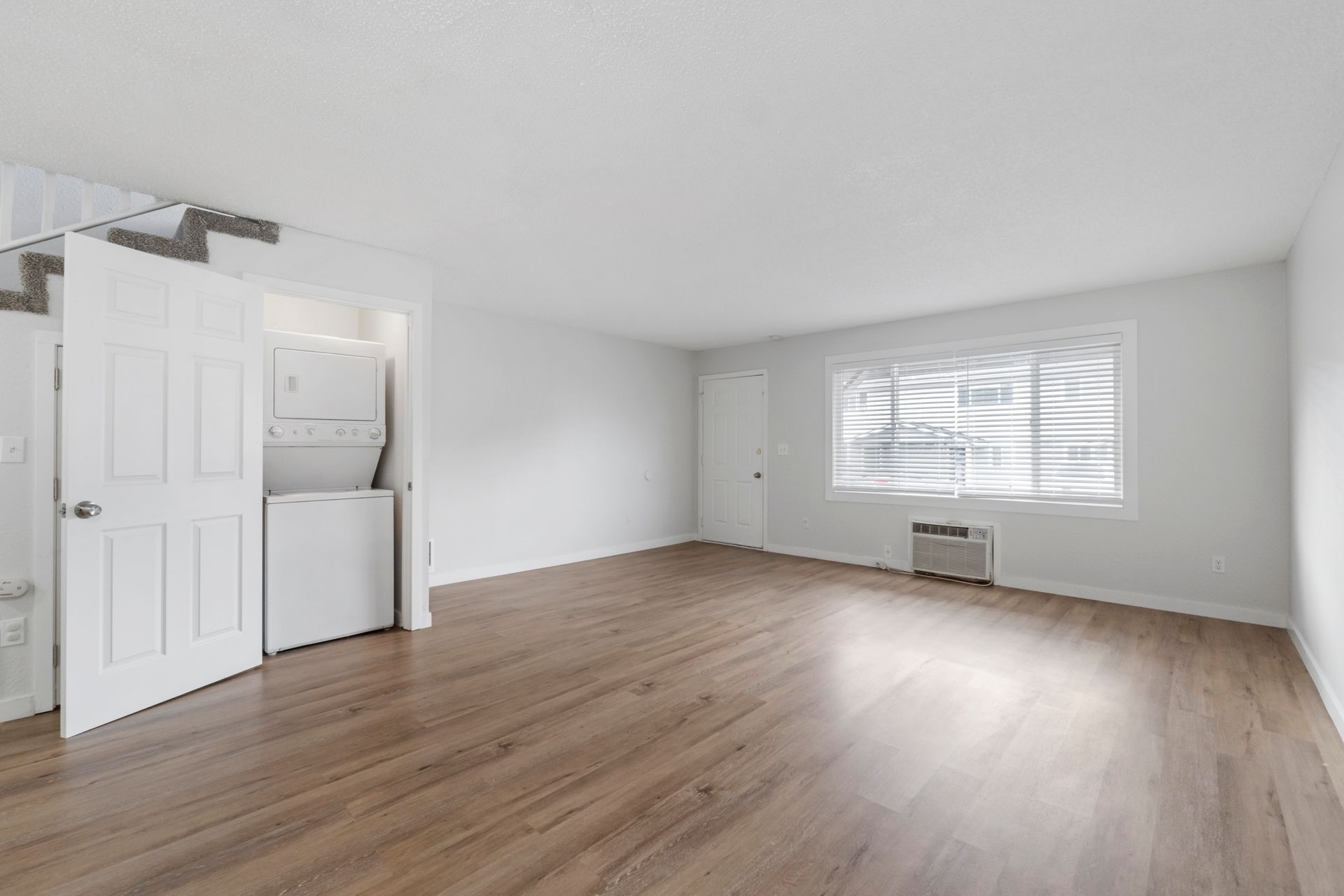 An empty living room with hardwood floors and a washer and dryer.
