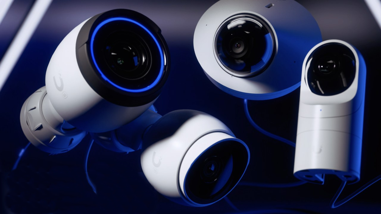 Four white security cameras on a reflective surface, lit with blue light.
