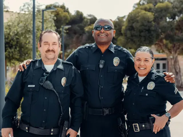 Three police officers in uniform, smiling and posing outdoors.
