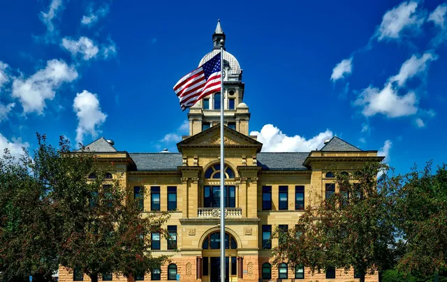 Yellow courthouse with American flag waving in front of a blue sky and white clouds.