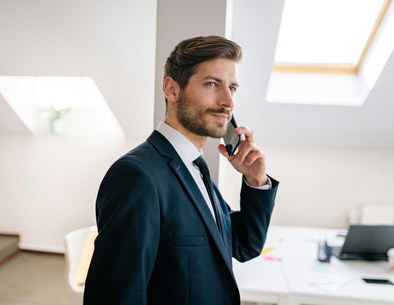 Man in a suit on a phone, looking over his shoulder in an office setting.