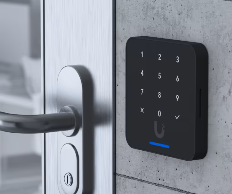 Black keypad smart lock on a gray concrete wall next to a silver door handle and door.