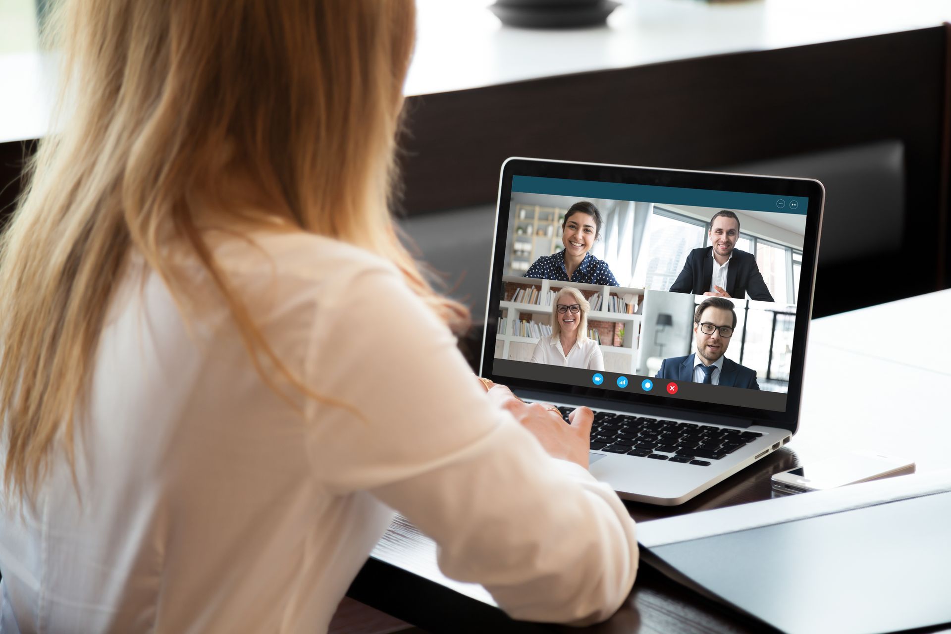 Woman at desk on laptop video call with three other people.