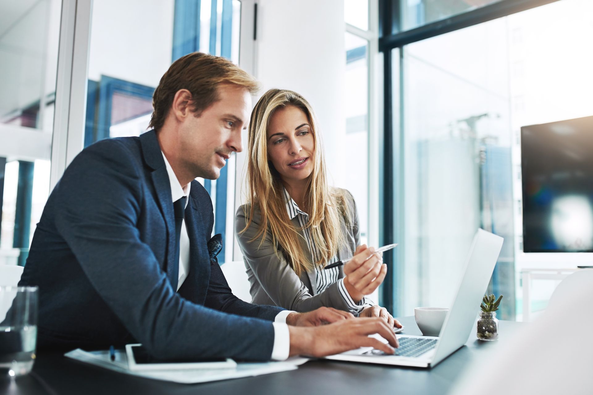 Man and woman in business attire looking at a laptop together at a desk.