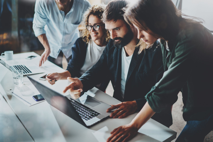 Group of people looking at a laptop, pointing, discussing project, in an office.