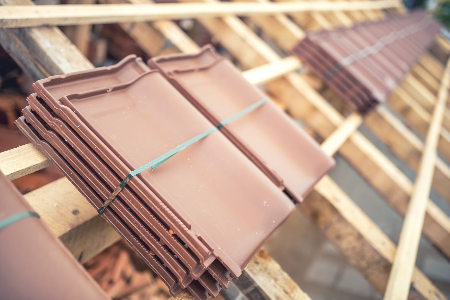 Stacked brown roof tiles tied with green straps on a wooden rack.