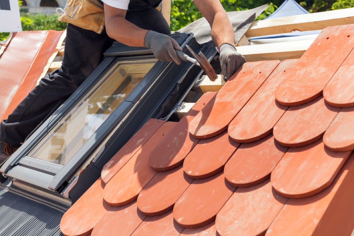 Worker installing a skylight on a red shingle roof with a caulking gun