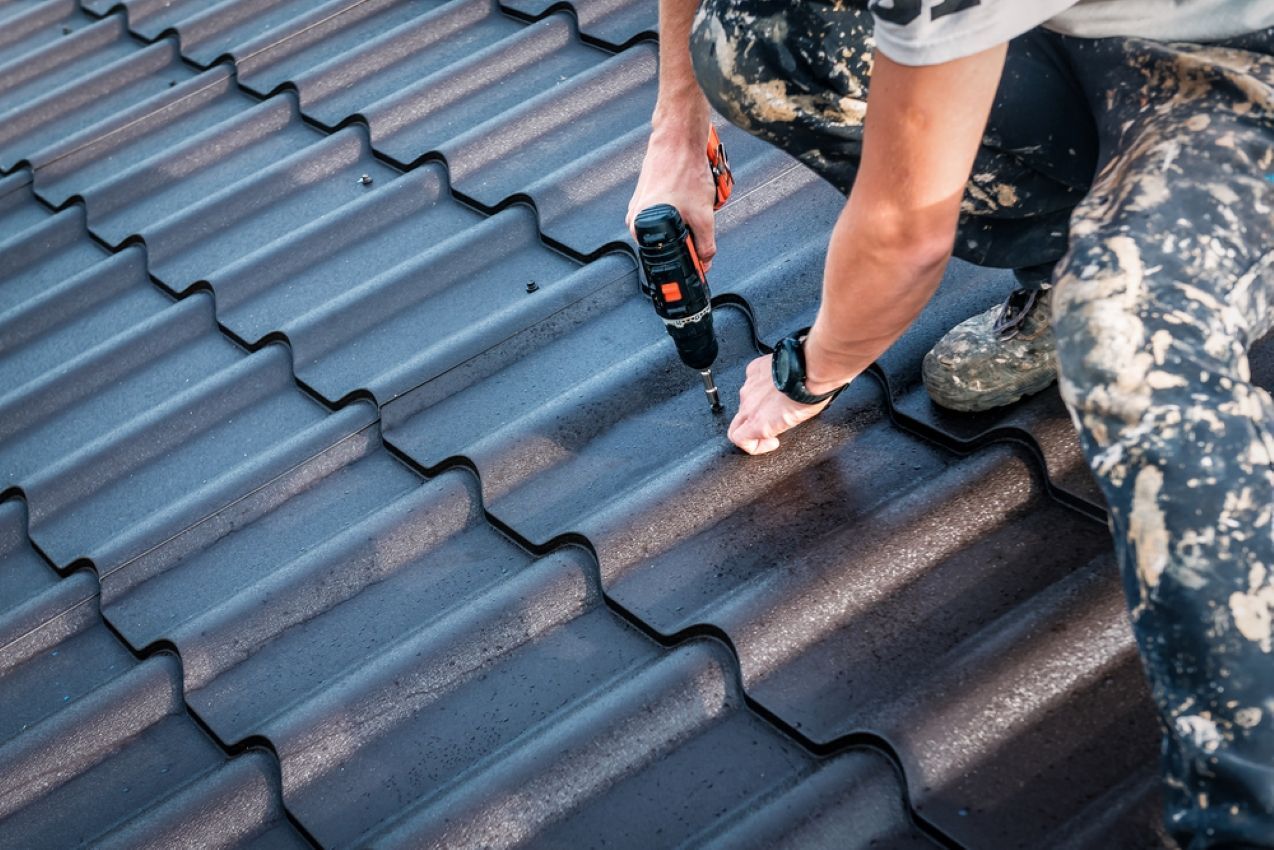 Worker drilling into dark roof tiles with a power tool