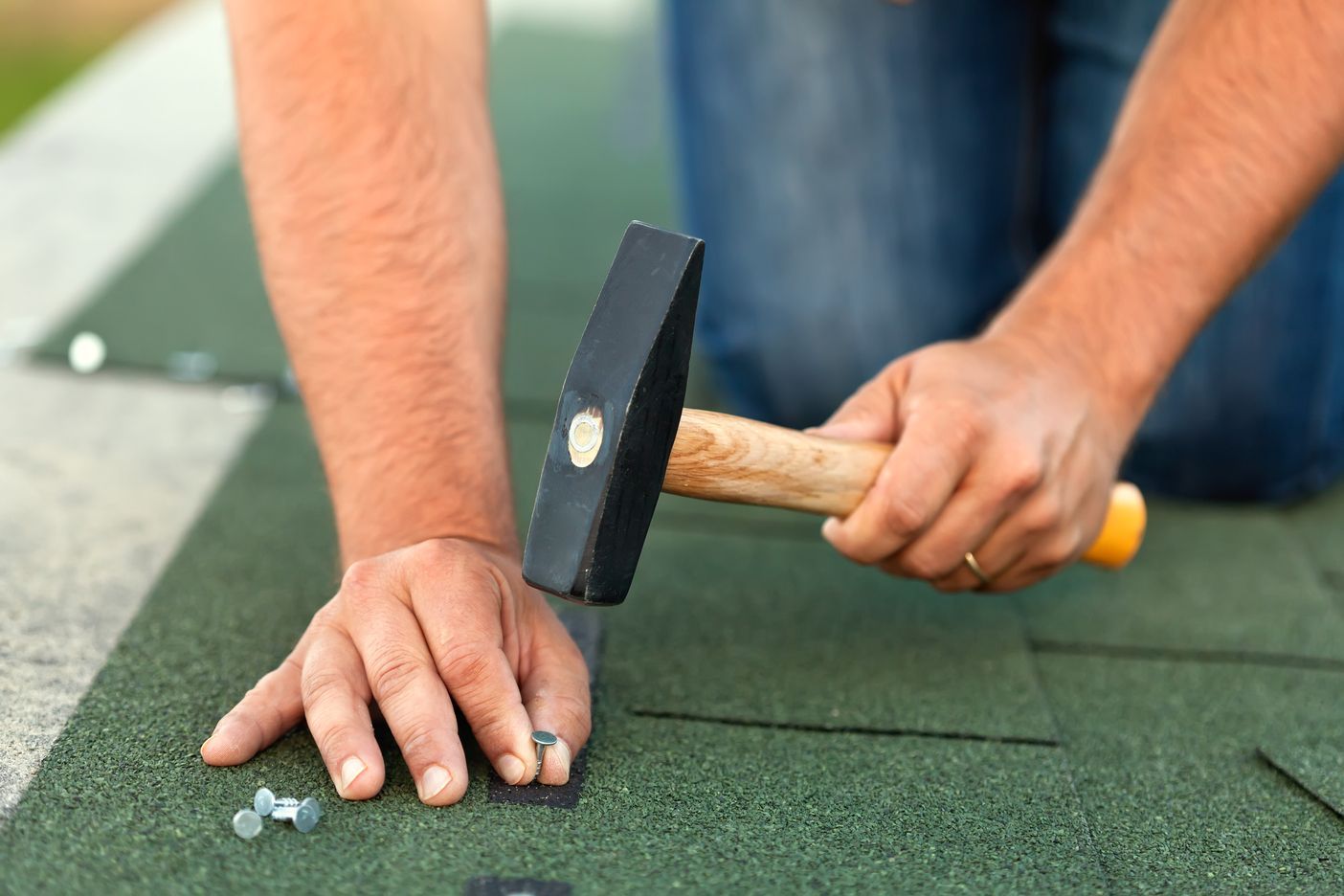Hands using a hammer to nail green roofing shingles into place