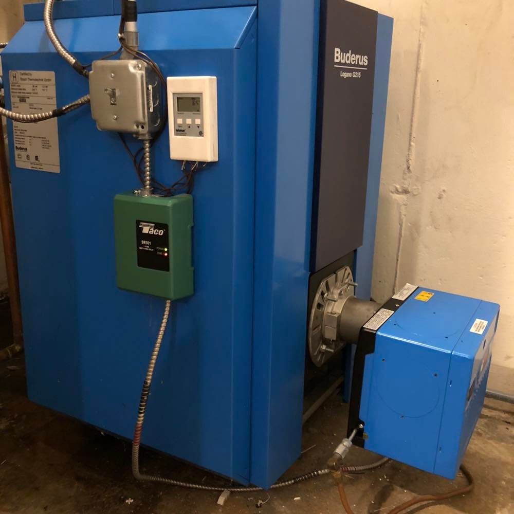 A blue Buderus Logano boiler with a mounted green control box and digital display, located in a mechanical room.