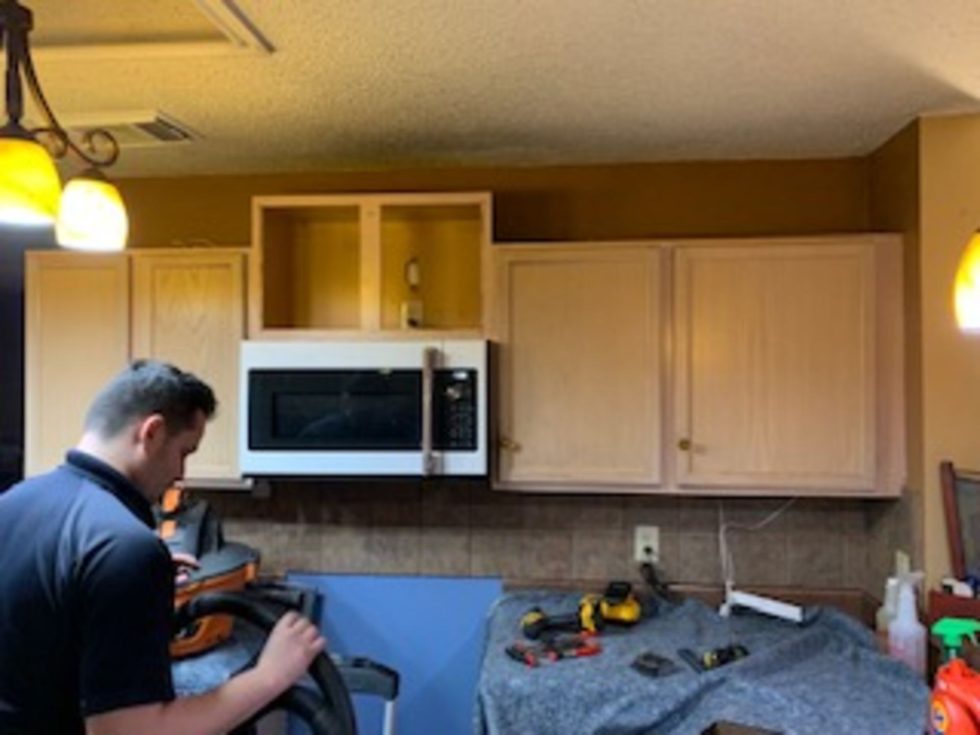 a man is working on a microwave in a kitchen .