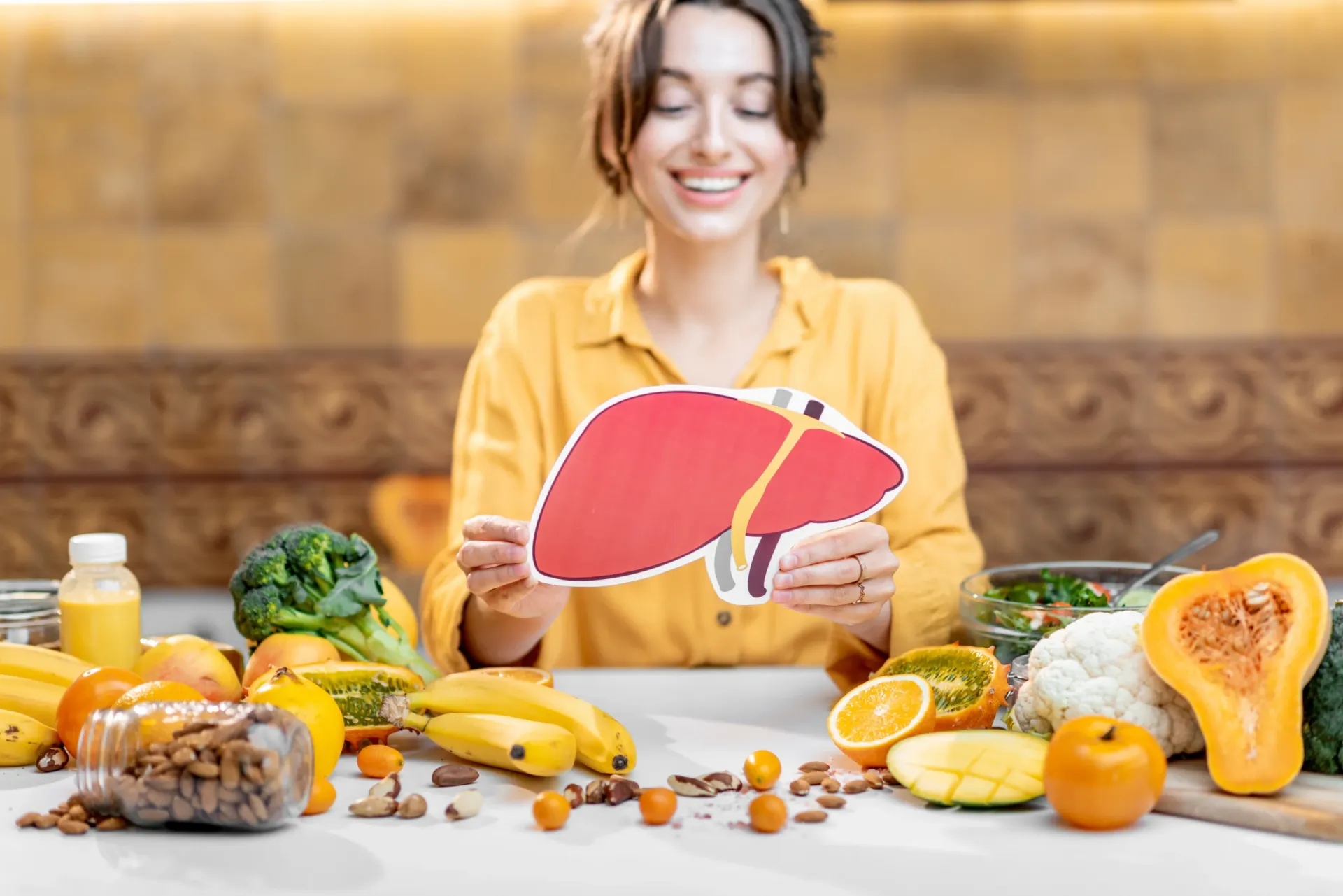 Woman holding a paper liver, surrounded by healthy foods, smiling.