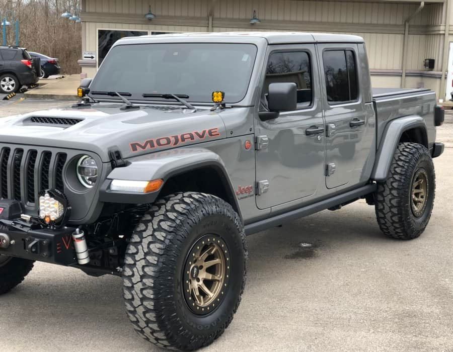 Gray Jeep Gladiator Mojave off-road vehicle with bronze wheels, parked in front of a building.