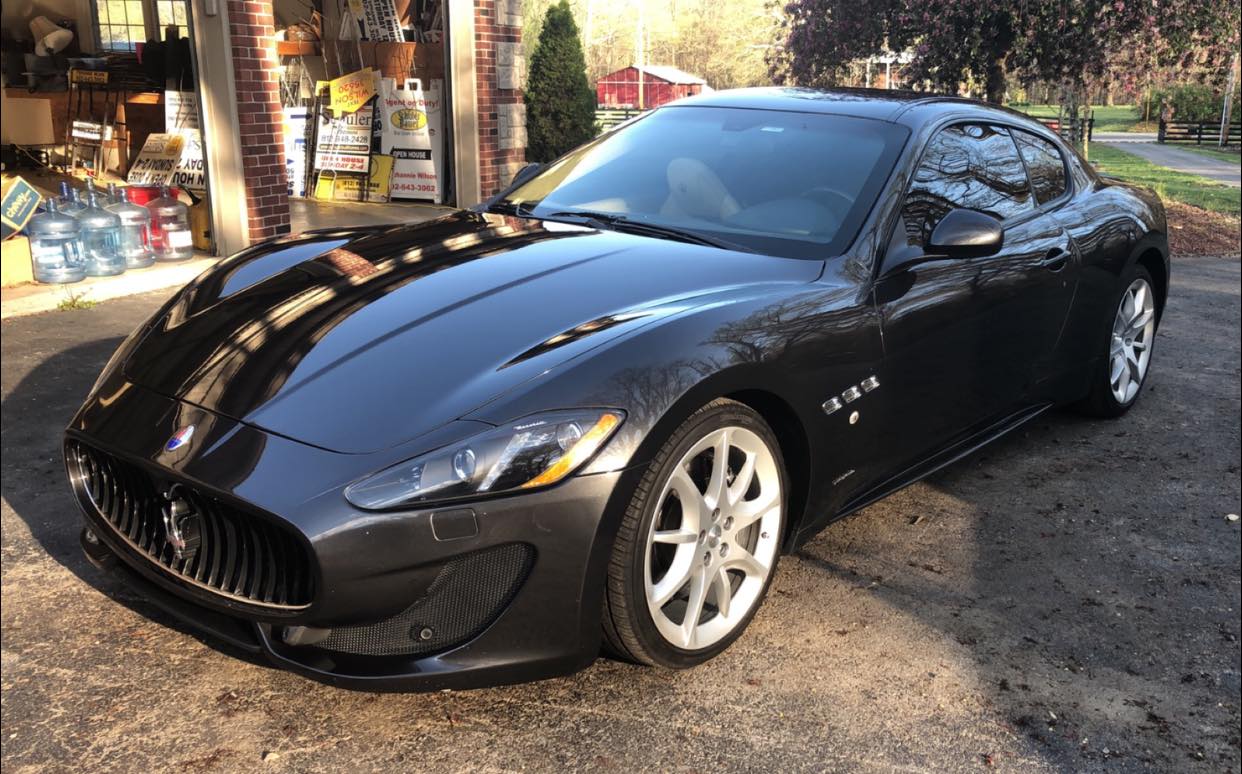 Dark gray Maserati GranTurismo coupe parked outdoors on a sunny day.