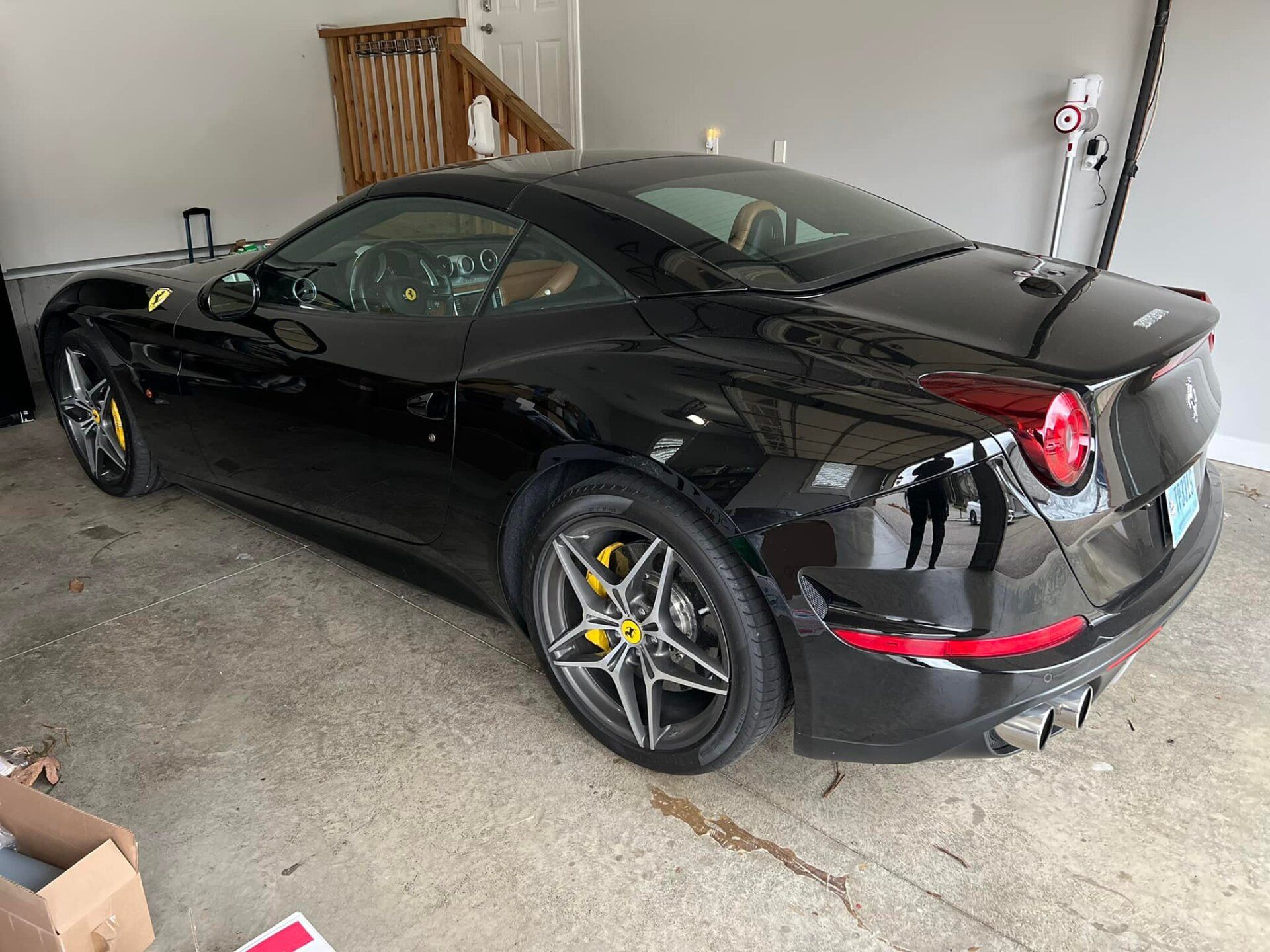 Black Ferrari parked in a garage, silver rims, yellow brake calipers, shiny body.