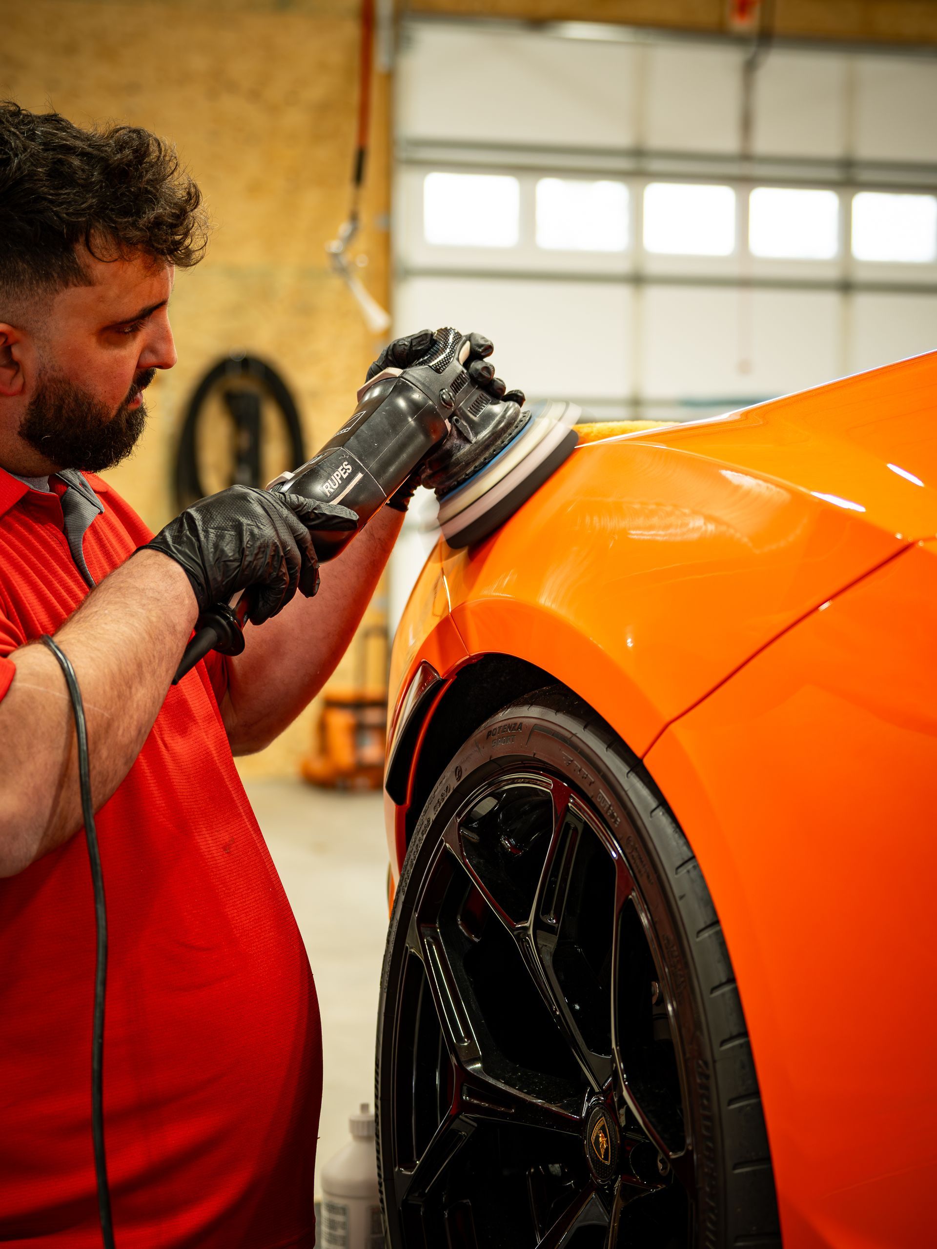 Man polishing bright orange car with black detailing.