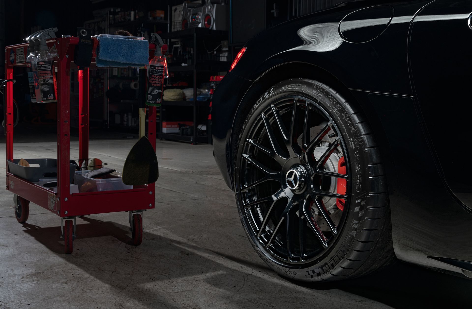 A black car is parked in a garage next to a red cart.