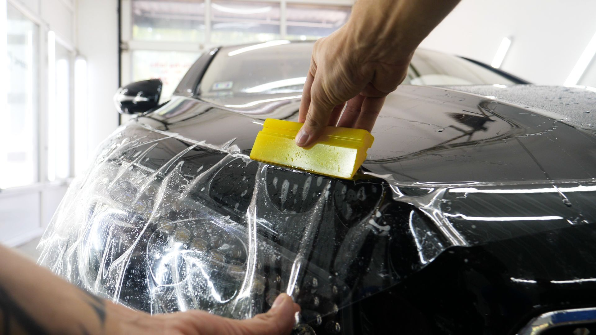 A person is applying protective film to the hood of a car.