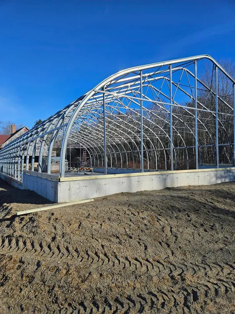 A large greenhouse is being built in the middle of a dirt field.