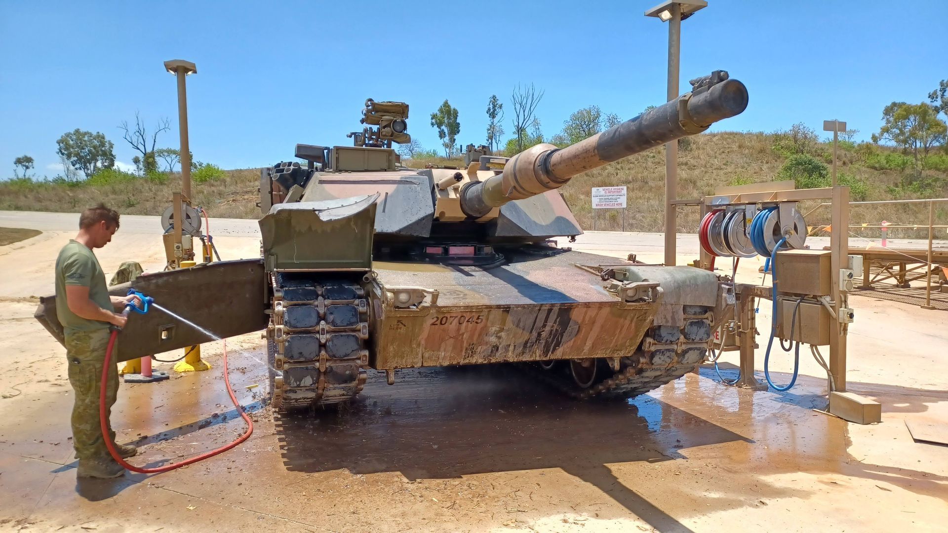 A Man Is Washing A Military Tank With A Hose — Eureka Water & Filtration In Mount St John, QLD