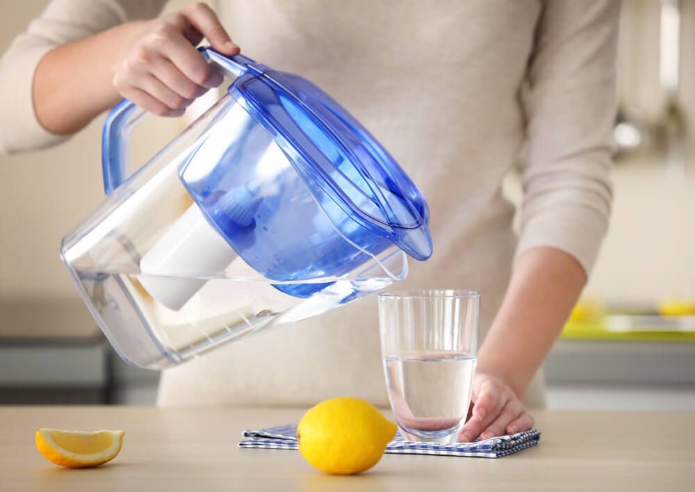 A Woman Is Pouring Water From A Pitcher Into A Glass — Eureka Water & Filtration In Cairns, QLD